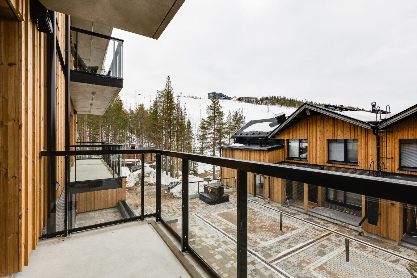 A modern wooden cabin with a balcony overlooking a snowy landscape and a ski slope.