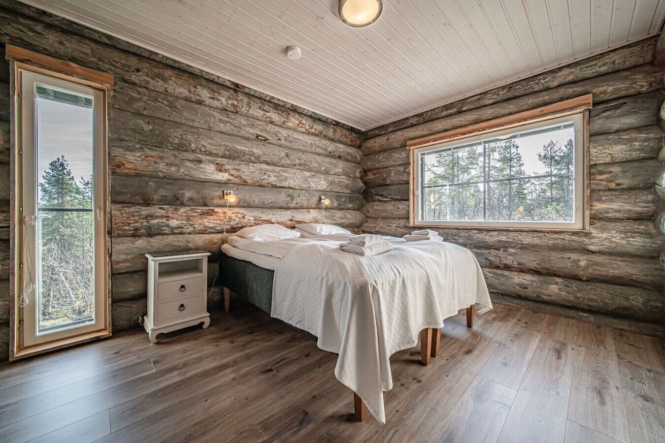 A log cabin bedroom with a bed, bedside tables, and a window with a view of trees.
