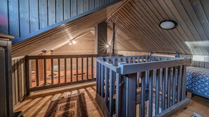 A loft bedroom with a sloped ceiling, wooden beams, a small balcony, and a patterned rug.