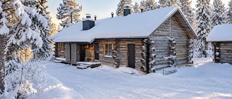 Une cabane en rondins dont le toit est recouvert de neige, entourée d’arbres chargés de neige.