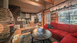 A cozy cabin interior with a red sofa, a dining area, and a kitchen.