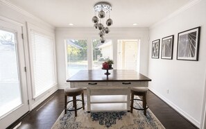 A kitchen with a dark wooden table, two stools, a chandelier, and framed pictures on the wall.