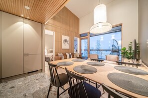 Un comedor moderno con techo de madera, ventanas grandes y vista a árboles cubiertos de nieve.