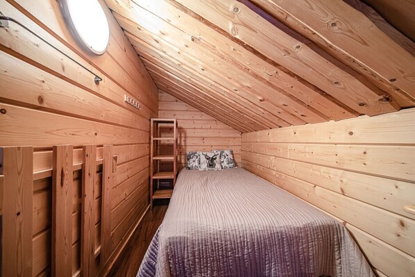A small, wooden cabin room with a bunk bed, a ladder, and a skylight.