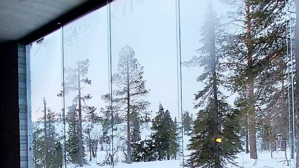 A modern interior with a glass fireplace, a metal table, and a view of a snowy forest. - Aavalevi Aurora Gielas, Top Of The Mountain (Levi)