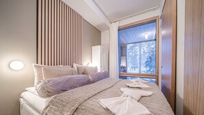 A bedroom with a large bed, a view of trees through a window, and a wooden slat wall. - Aavalevi Aurora Gielas, Top Of The Mountain (Levi)