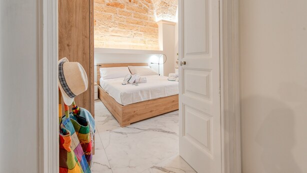 Une chambre avec un lit en bois, un mur blanc, un plafond en briques et une porte.