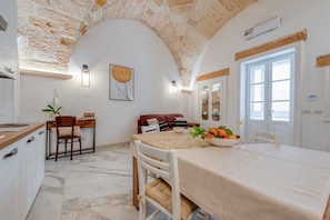 Un coin repas avec une table dressée pour quatre personnes, une cuisine dotée d’un plan de travail en marbre et un plafond en forme d’arc en pierre.