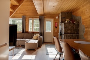 A cozy cabin interior with a wooden ceiling, a stone fireplace, a sofa, and a dining table.