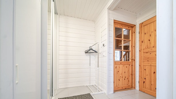 Bagno con pareti bianche, una doccia, porta asciugamani e una porta in legno.