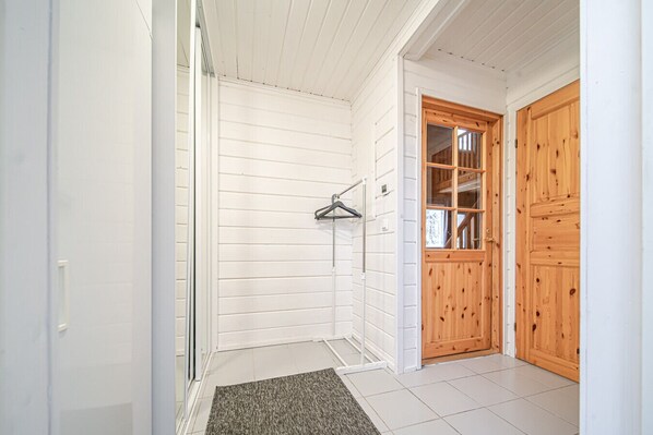 A bathroom with white walls, a shower, a towel rack, and a wooden door.