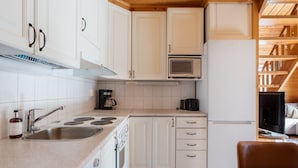 Una cucina compatta con mobili bianchi, forno a microonde integrato, macchina da caffè e frigorifero.