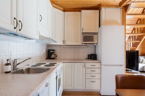 Cocina compacta con gabinetes blancos, microondas integrado, cafetera y refrigerador.