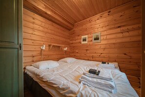 A wooden cabin room with a bed, two bedside lamps, and two framed pictures on the wall.