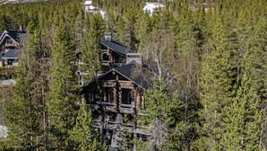 Eine Blockhütte mit steilem Dach, umgeben von dichtem Wald, mit einem Berg im Hintergrund.