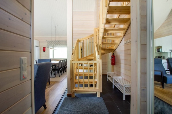A wooden interior with a staircase, a dining area, and a kitchen visible through an open door.