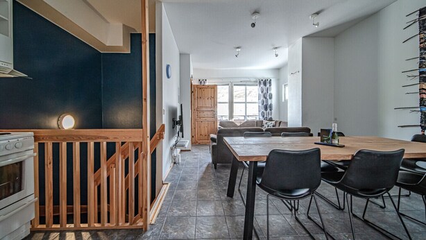 Eine moderne Küche mit einer Holztreppe, einem Essbereich mit schwarzen Stühlen und einem großen Fenster.