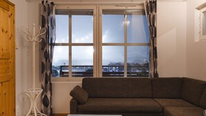 Ein Wohnzimmer mit einem braunen Sofa, einem weißen Tisch und einem Fenster mit Vorhängen.