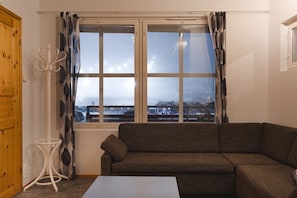 Un salon avec un canapĂ© marron, une table blanche et une fenĂȘtre avec des rideaux.