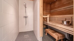 Una sauna con banco de madera, estante de madera con una olla y zona de ducha con suelo de baldosas.