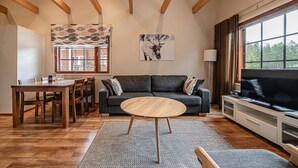 Una sala de estar con una mesa de comedor de madera, un sofá gris, una mesa redonda de centro y un televisor grande.