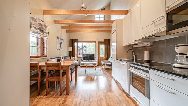 Una cocina moderna con vigas de madera, un comedor con mesa y sillas, y vistas al exterior a través de amplios ventanales.