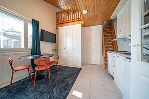 Eine kleine Küche mit weißen Schränken, einer Holztreppe und einem Essbereich mit Tisch und Stühlen.