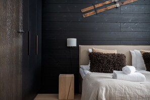 A bedroom with a dark wooden wall, a bed with white and brown pillows, a bedside lamp, and a wooden nightstand.