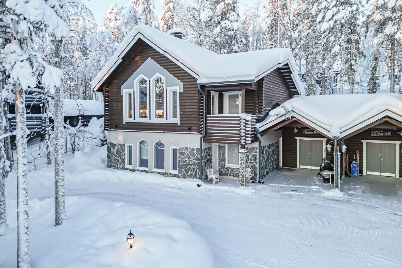 En timmerstuga med en fasad av sten, stora fönster och ett snötäckt tak.