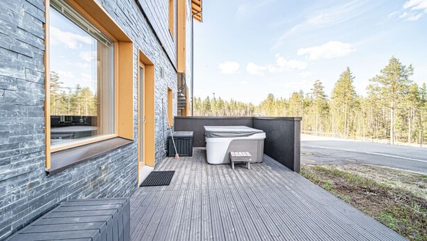 Un edificio moderno con terraza de madera, jacuzzi y vistas a un bosque.