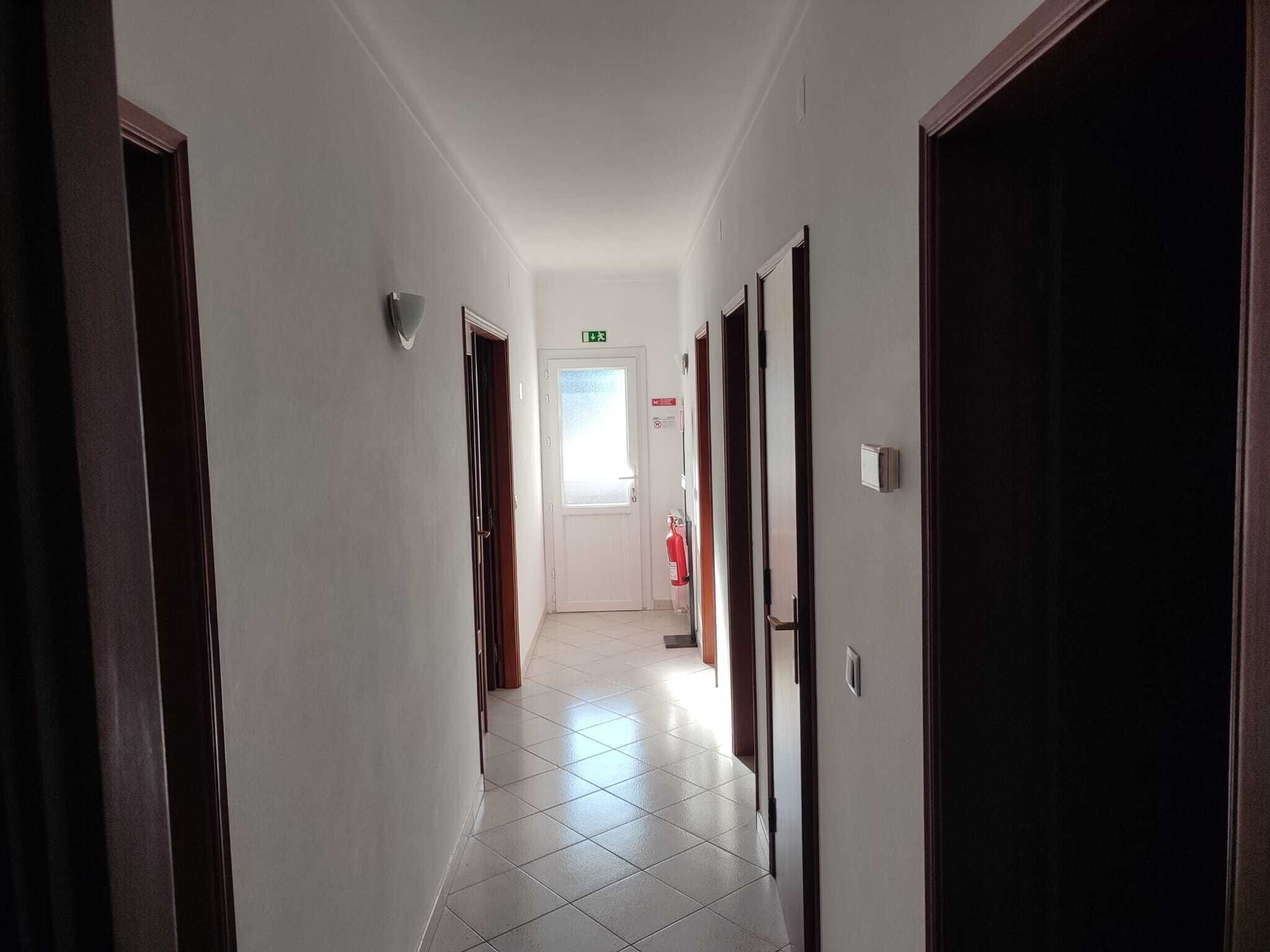 Un pasillo largo y estrecho con pisos de baldosas blancas y puertas de madera a ambos lados.