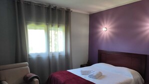 A hotel room with a bed, a chair, a nightstand, and a window with curtains. - Casa dos Fetos - Rural vacation home in Portugal (Espite)