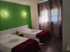 Ein Zimmer mit zwei Betten, grünen Wänden und einem Fenster mit gestreiften Vorhängen.