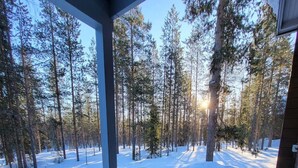 Une terrasse en bois avec un banc, entourée d’une forêt enneigée.