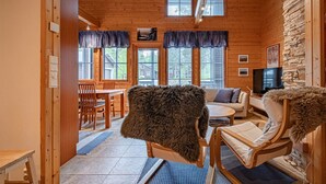 L’intérieur chaleureux d’un chalet avec un coin repas en bois, un canapé, un téléviseur et un mur en pierre.
