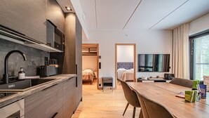 Una habitación de hotel compacta con kitchenette, zona de comedor, cama y televisor.