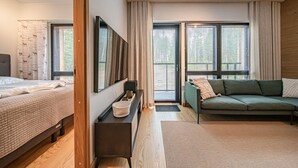 Un dormitorio moderno con cama, sofá, un ventanal con cortinas y suelo de madera.