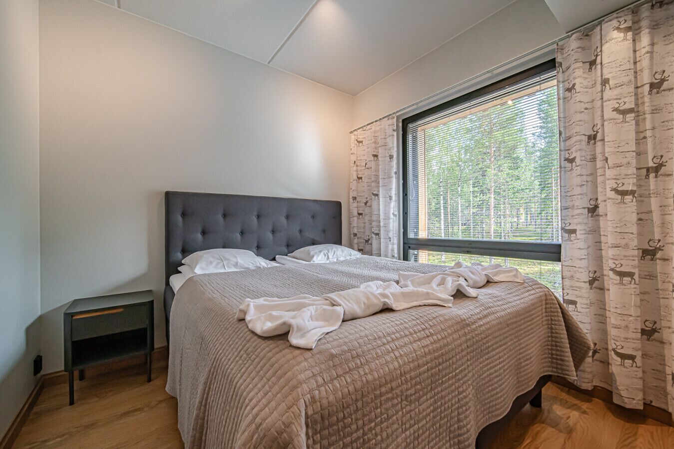 Een slaapkamer met een groot bed, een nachtkastje en een raam met gordijnen.