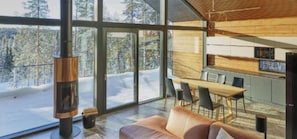 A modern interior with a fireplace, large windows, a dining area, and a kitchen.