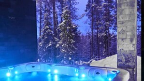 A hot tub with a blue-lit interior, surrounded by a snowy forest.