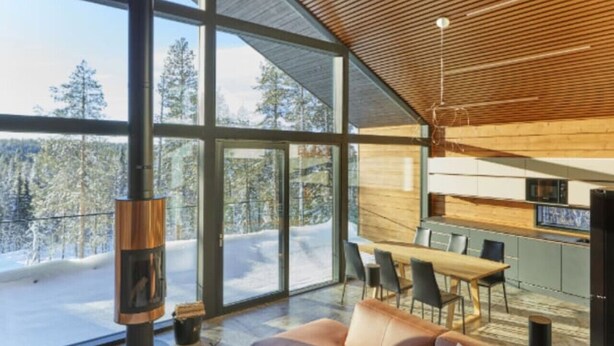 A modern interior with a large glass window, a cozy brown sofa, a dining area, and a kitchen.