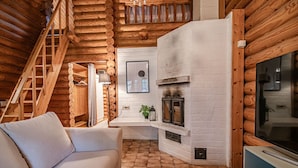 Ein Holzblockhaus-Innenraum mit einem weißen Sofa, einem Kamin, einem Fernseher und einer Holztreppe.