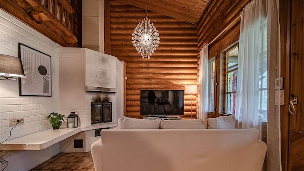 Ein gemütliches Blockhaus-Interieur mit einem weißen Sofa, einer Holzbalkendecke und einem Kamin.