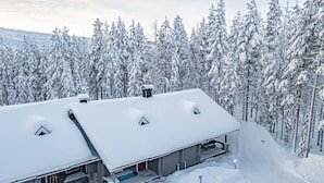 Ein mit Schnee bedecktes Gebäude mit geneigtem Dach, umgeben von dicht bewachsenen, schneebedeckten Bäumen.