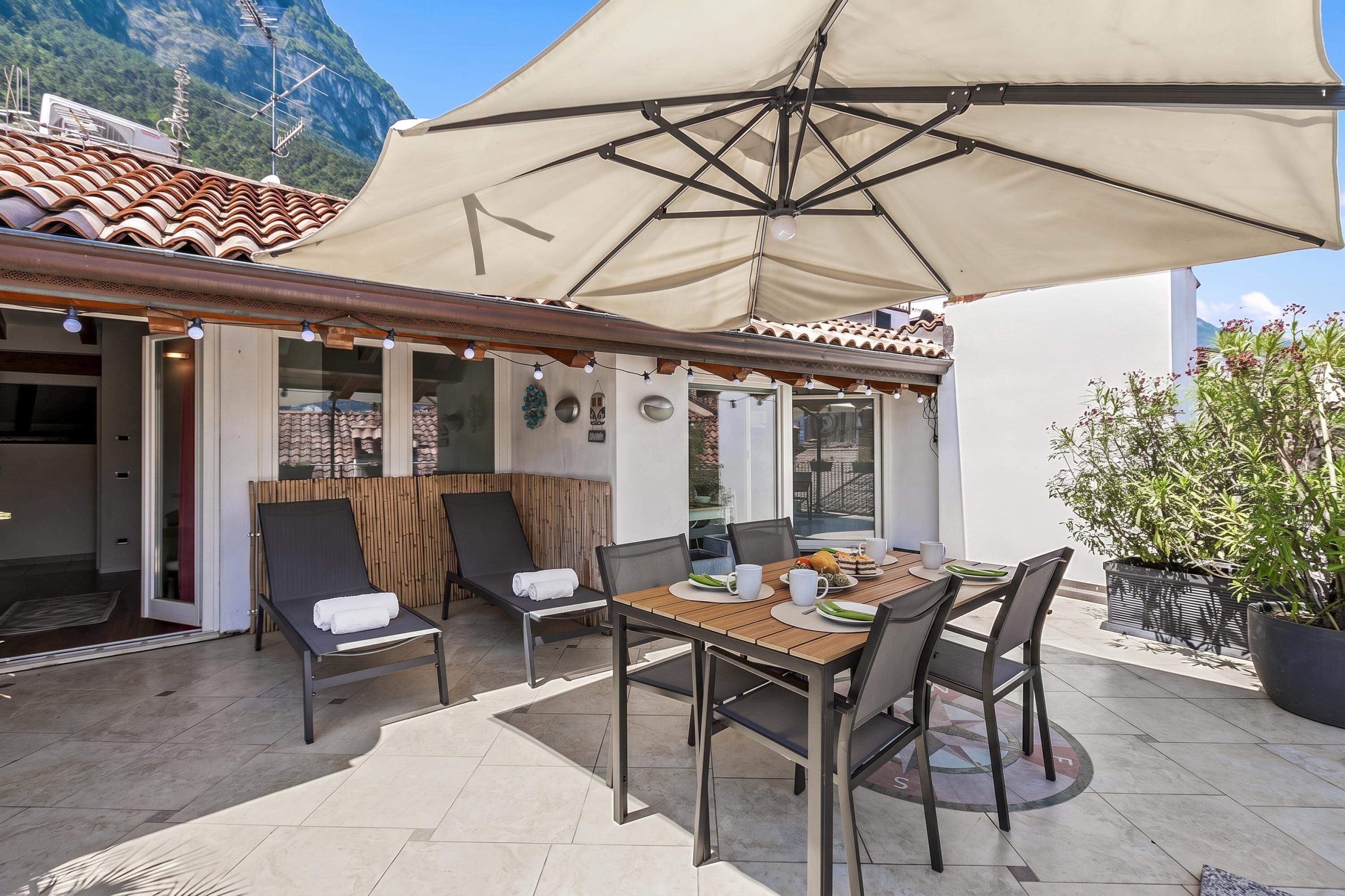 Patio esterno con tavolo, sedie e un ombrellone grande.