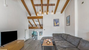 Un salon moderne doté d’un grand téléviseur à écran plat, d’une table basse en bois, d’un canapé d’angle gris et de poutres apparentes en bois au plafond.