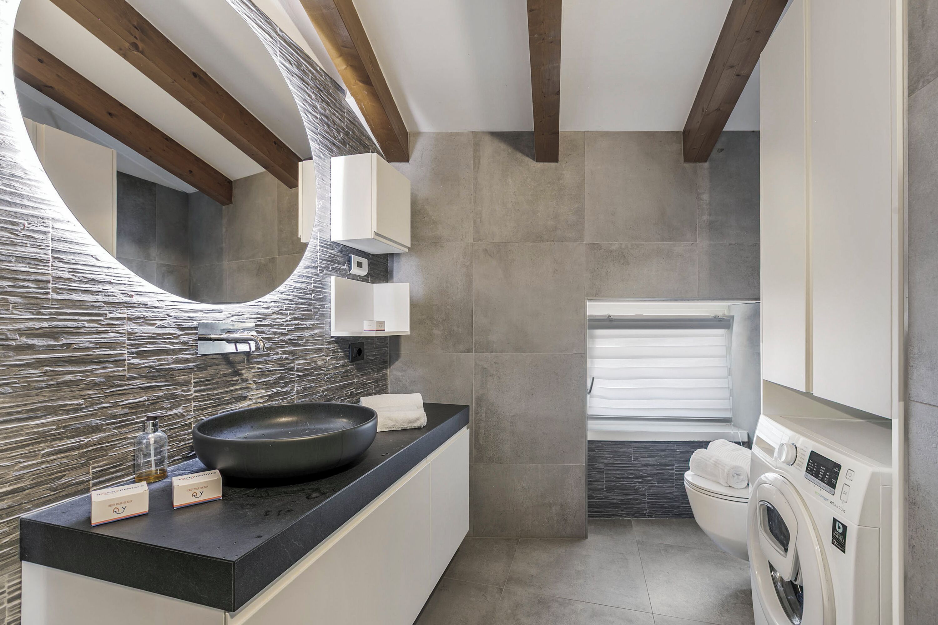Een moderne badkamer met een stenen spatwand, een ruime wastafel, een toilet en een wasmachine.