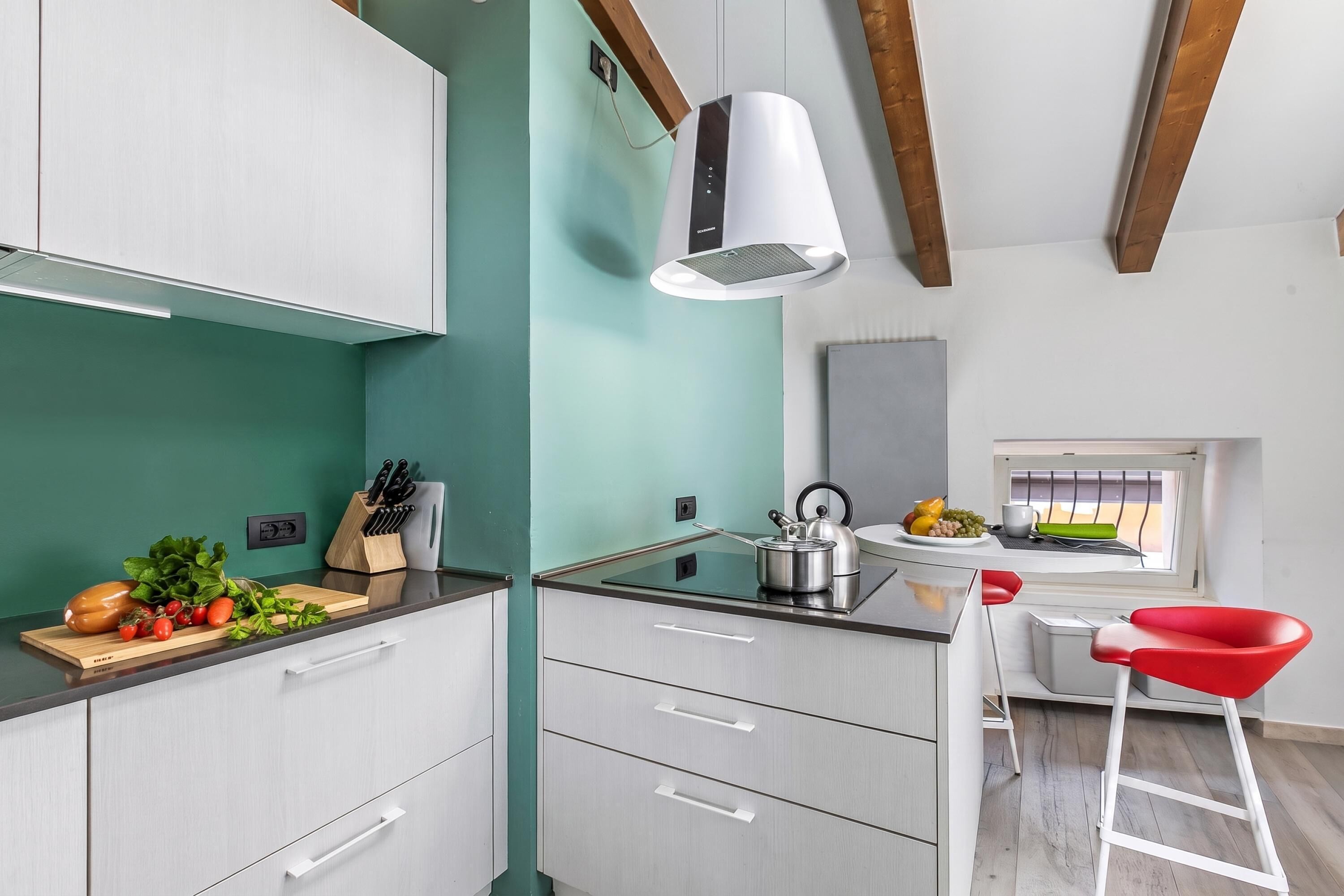 A modern kitchen with white cabinetry, a stainless steel kettle, and a red chair.