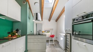 Une cuisine moderne avec des meubles blancs, un îlot central, un tabouret rouge et une lucarne.