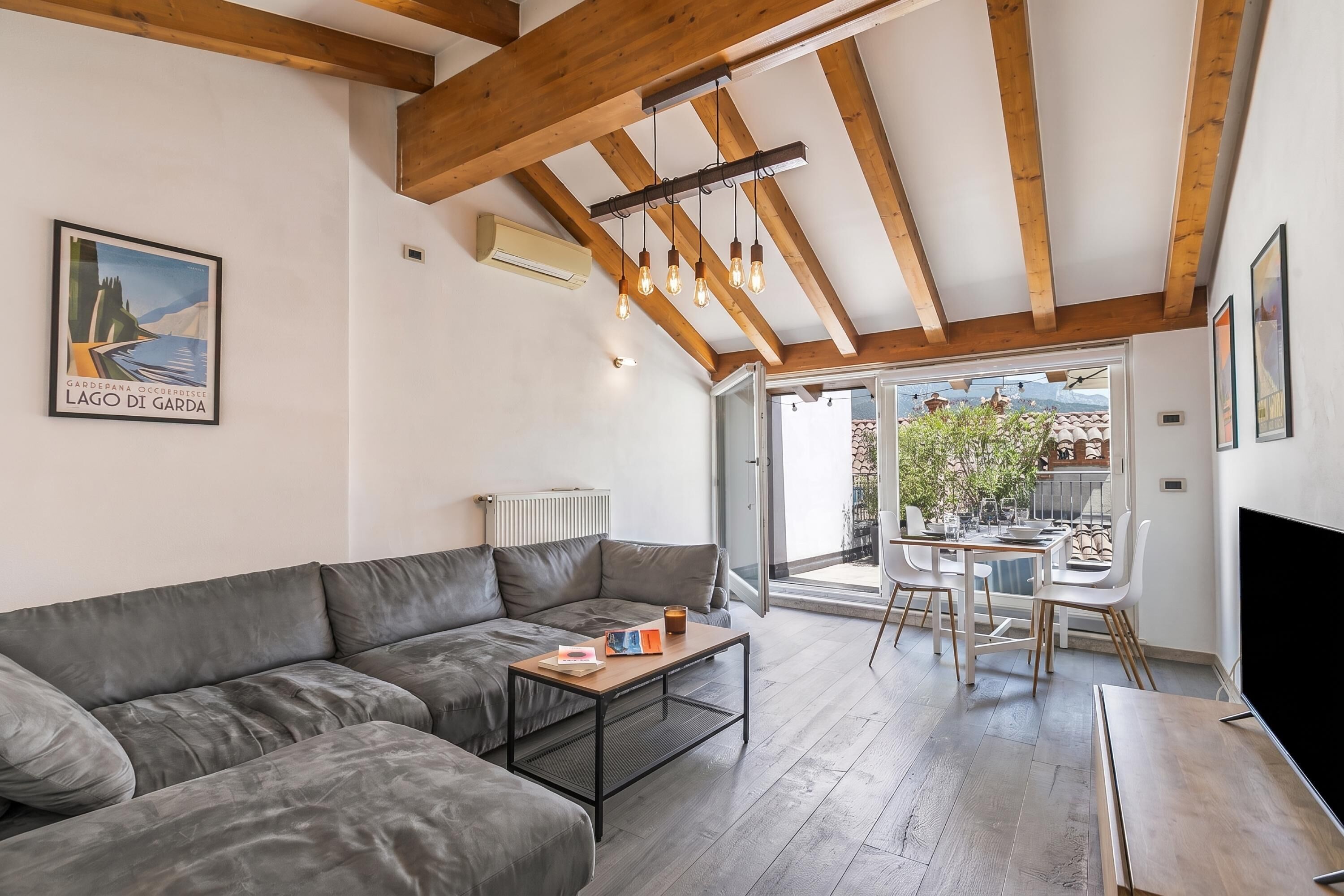 Ein modernes Wohnzimmer mit grauem Sofa, einem Couchtisch und einem Essbereich mit weißen Stühlen.